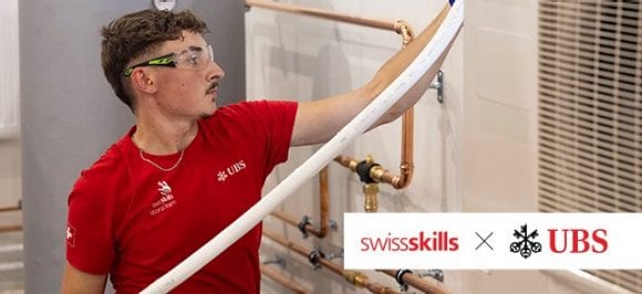 Un apprenti chauffagiste en train d'installer une conduite dans une cave. Il porte un t-shirt rouge SwissSkills.